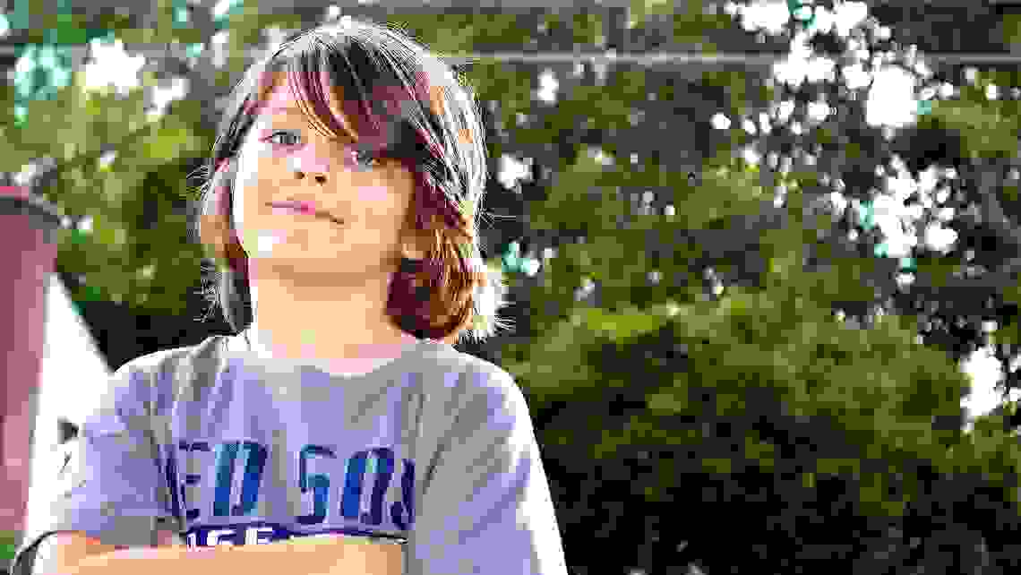 En pojke med brunt långt hår håller armarna i kors. 