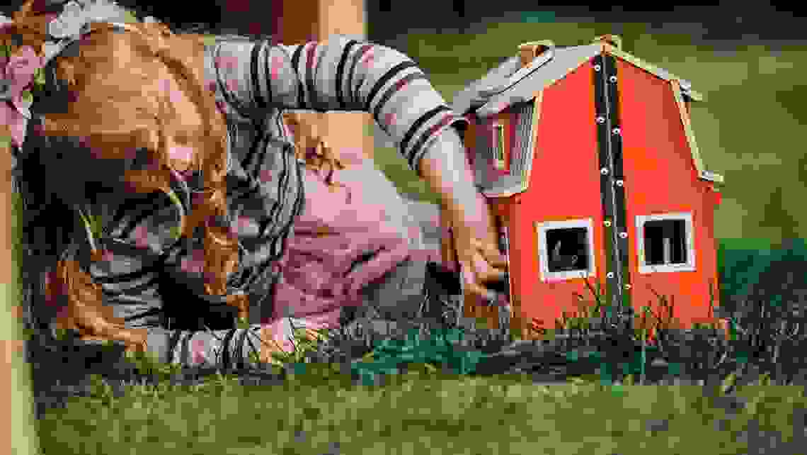 Flicka i förskoleåldern leker med ett dockhus utomhus.
