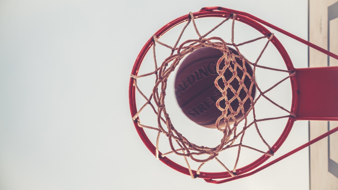 En basketkorg sedd underifrån med en basketboll på väg igenom.