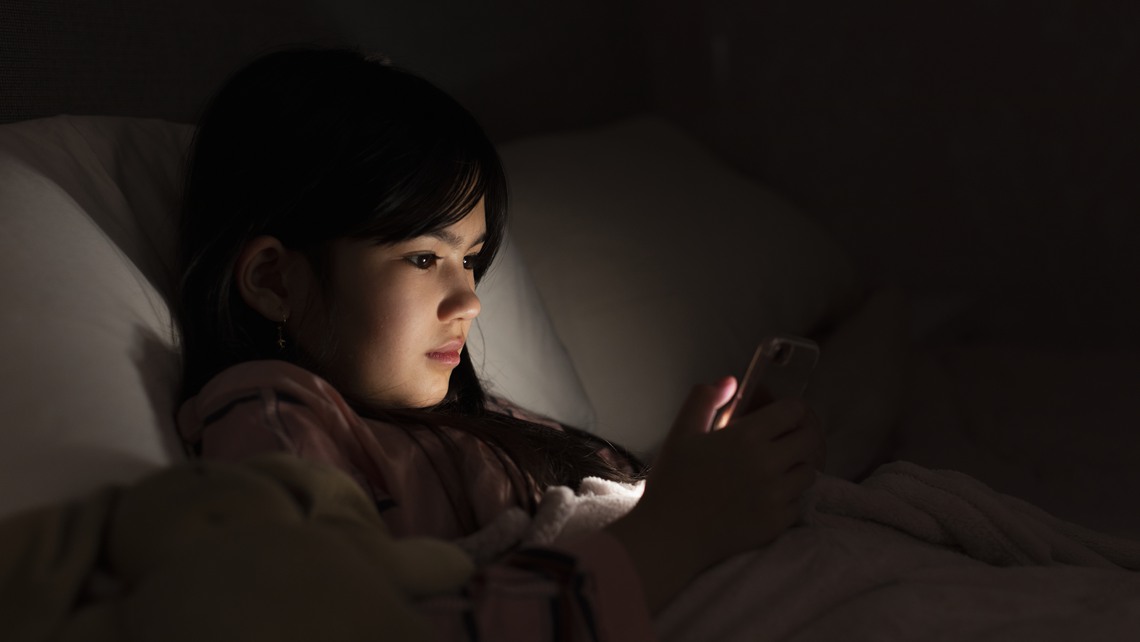 Ung tjej med mobil i sängen