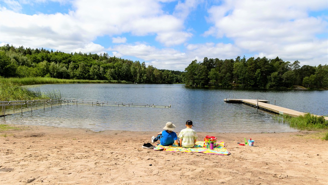 Barn sitter på en filt på stranden och tittar ut över sjön.