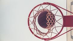 En basketkorg sedd underifrån med en basketboll på väg igenom. 