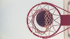 En basketkorg sedd underifrån med en basketboll på väg igenom.