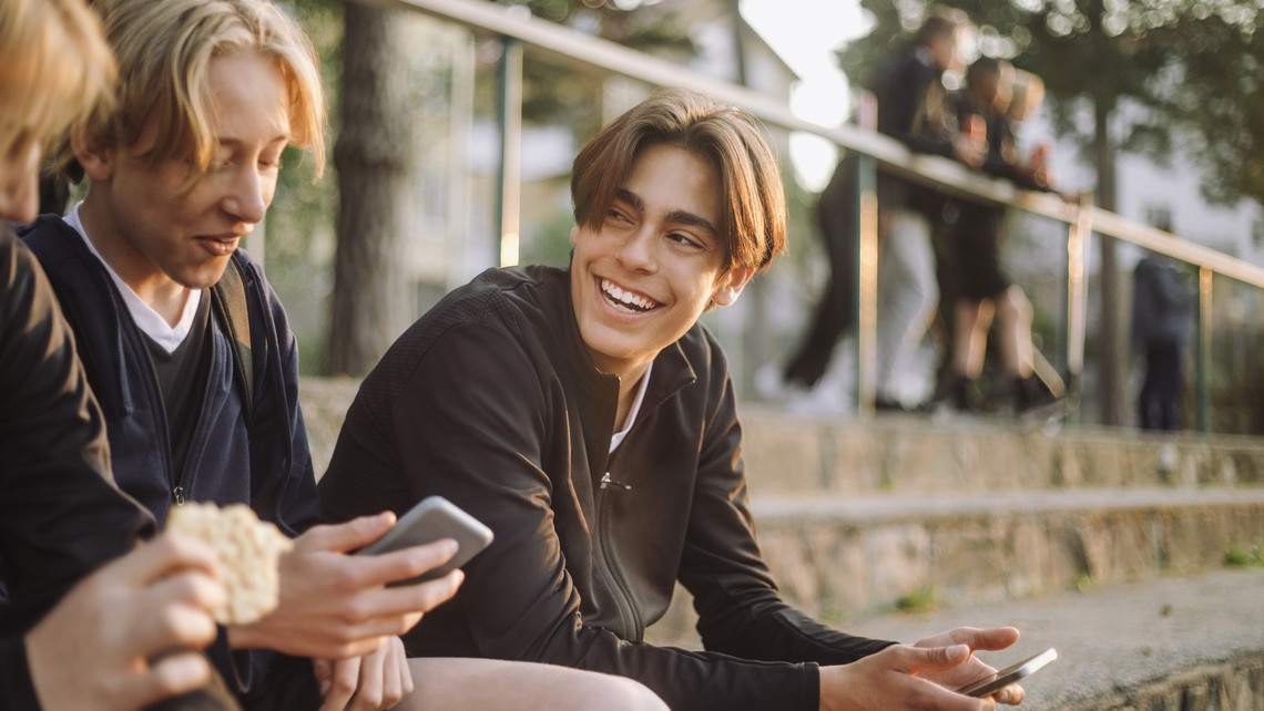 Glad ung kille håller i smartphone och pratar med kompisar