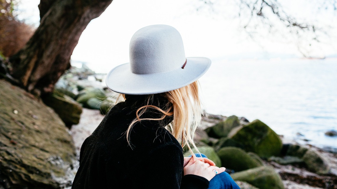 En kvinna sitter med en hatt och blickar ut över havet. 