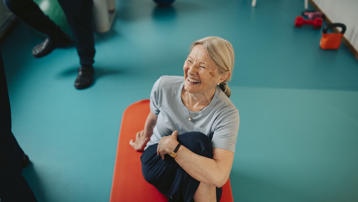 High angle view of happy senior woman stretching while sitting on exercise mat at retirement home