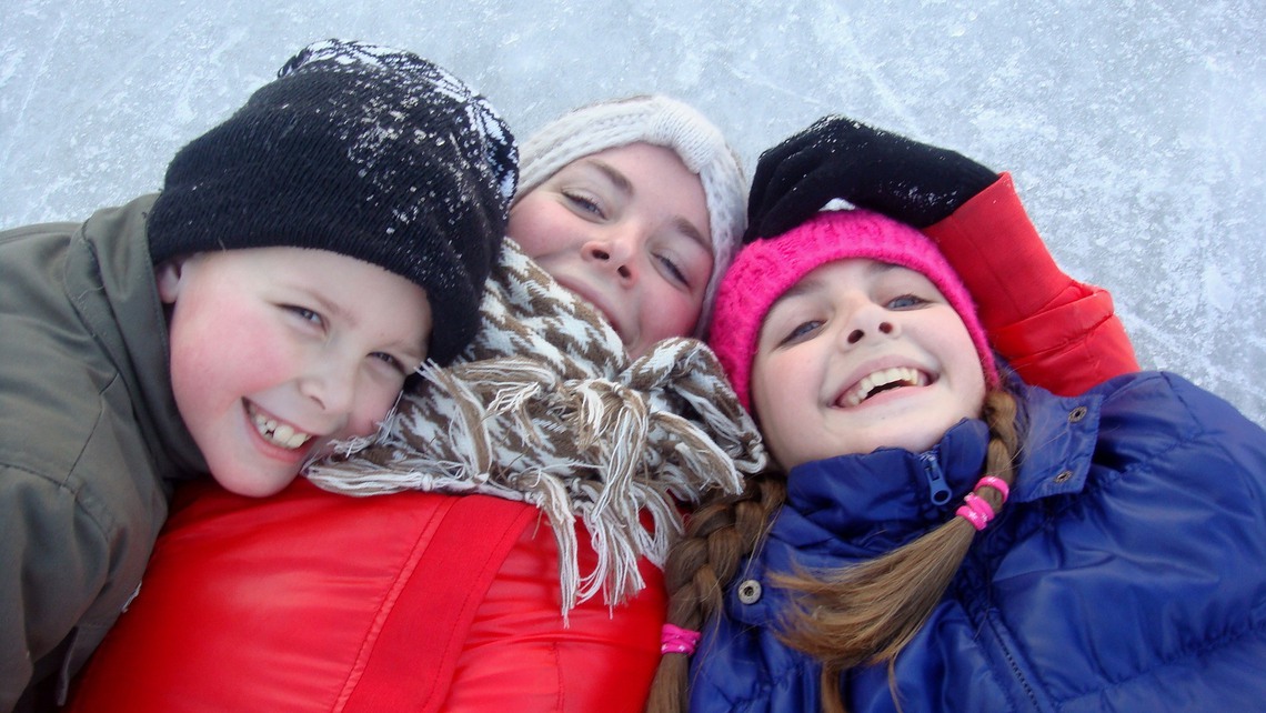 Tre barn ligger på isen och skrattar. 