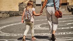 Flicka håller sin mamma i handen när de går över skolgården.