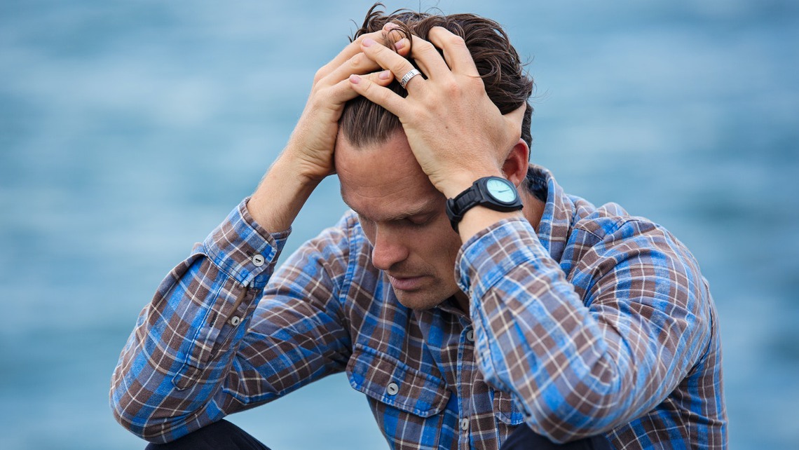 Man som ser stressad ut sitter nära vatten.  