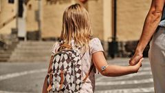 Flicka håller sin mamma i handen när de går över skolgården.