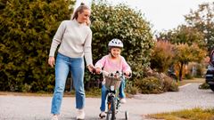 Flicka cyklar med mamma i bakgrunden
