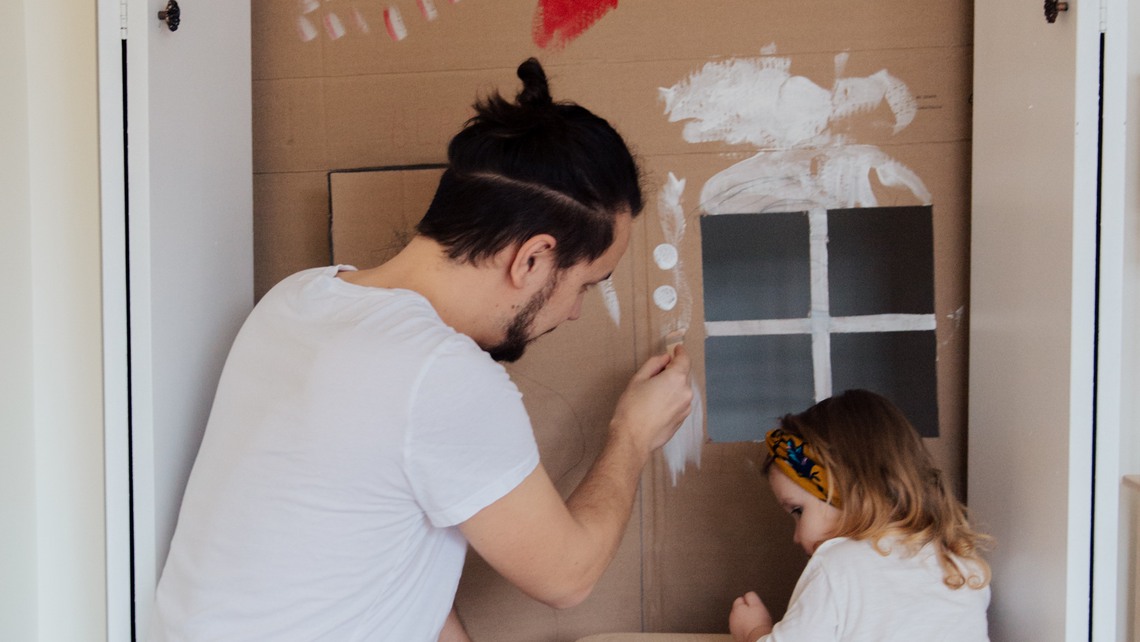 En pappa och hans dotter bygger ett hus av papp. 