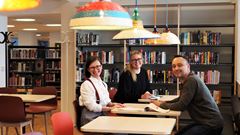 Två kvinnor och en man sitter vid bord i biblioteket i Mörby centrum och är glada