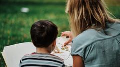 En kvinna sitter utomhus och läser en bok för en pojke.