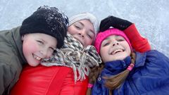 Tre barn ligger på isen och skrattar.