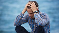 Man som ser stressad ut sitter nära vatten.