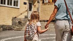 Flicka håller sin mamma i handen när de går över skolgården.