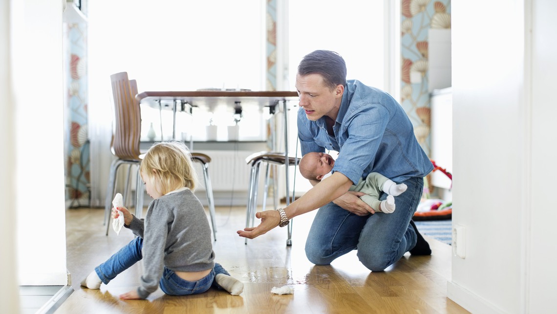Father holding baby girl while cleaning floor with daughter at home