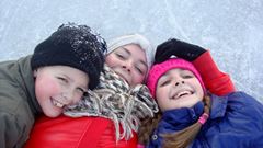 Tre barn ligger på isen och skrattar. 