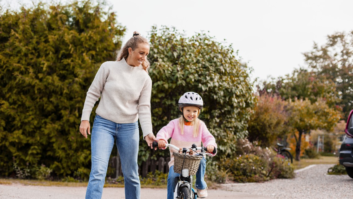 Flicka cyklar med mamma i bakgrunden