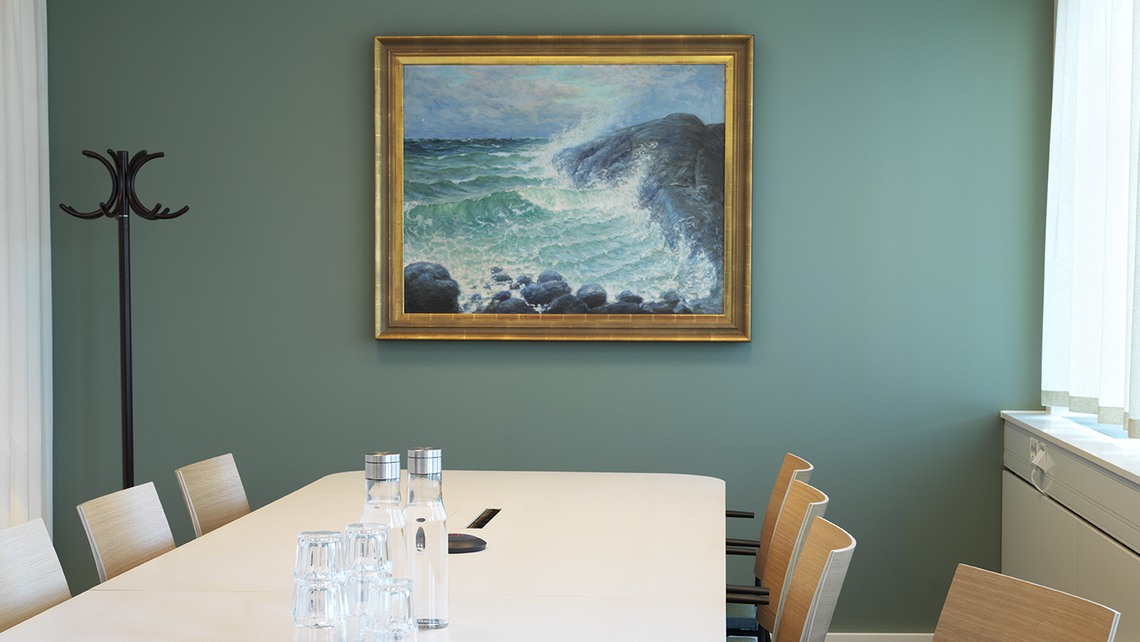 Mötesrum i Mötesparken, Mörby centrum. Konferensbord med stolar, på den gröna väggen hänger en tavla med havsmotiv.