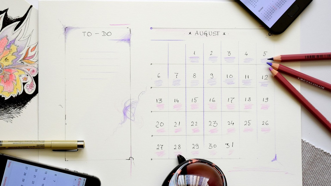 En kalender ligger på ett bord med två mobiler intill som också har kalendern uppslagen. 