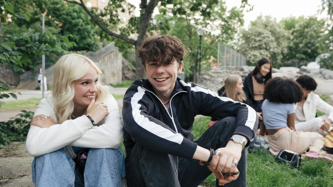 Portrait of smiling teenage boy sitting by blond girl with friends in background
