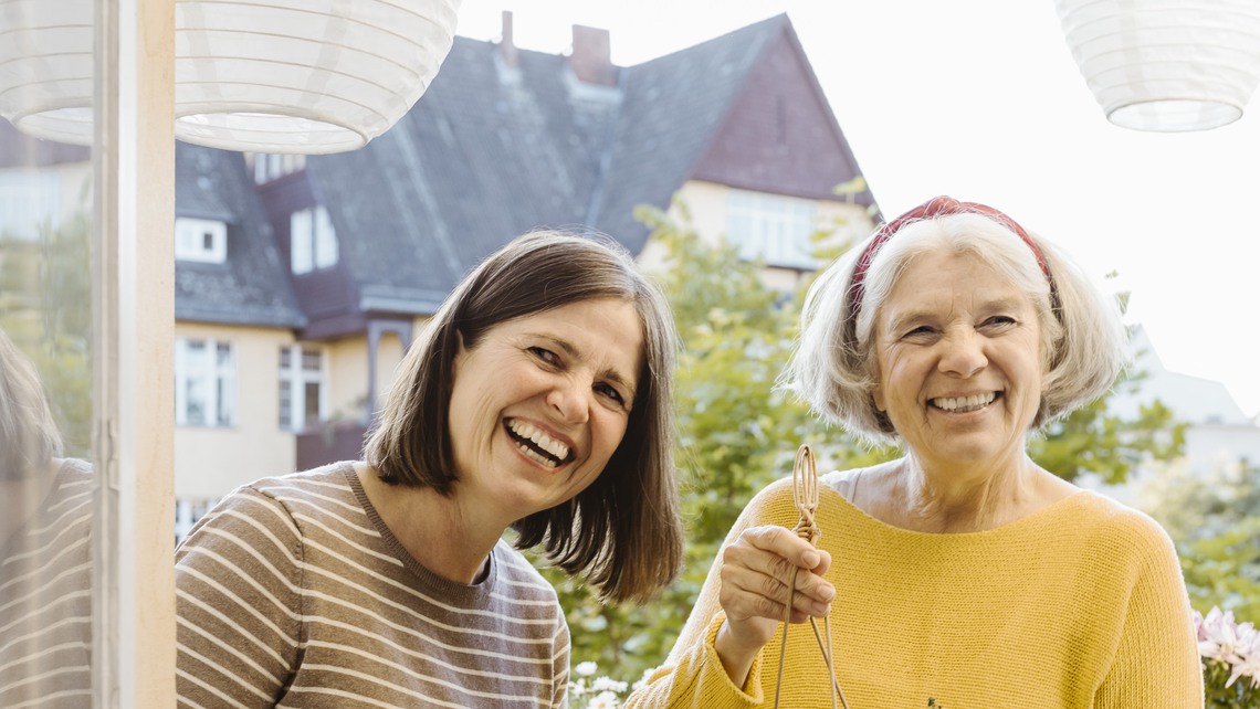 Happy woman and mother-in-law holding potted plant in balcony