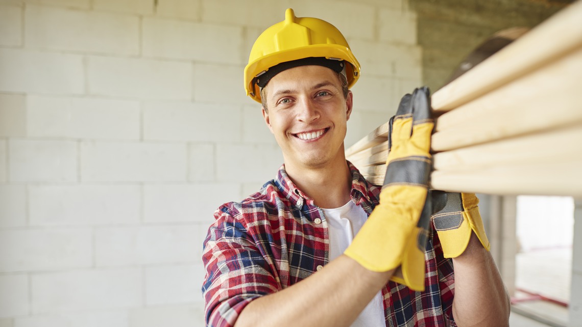 Ung kille i snickarkläder som bär tre plankor.