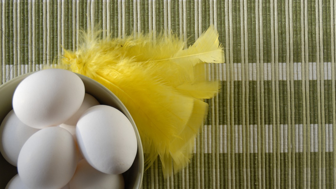 En skål med ägg och påskfjädrar på grön duk.