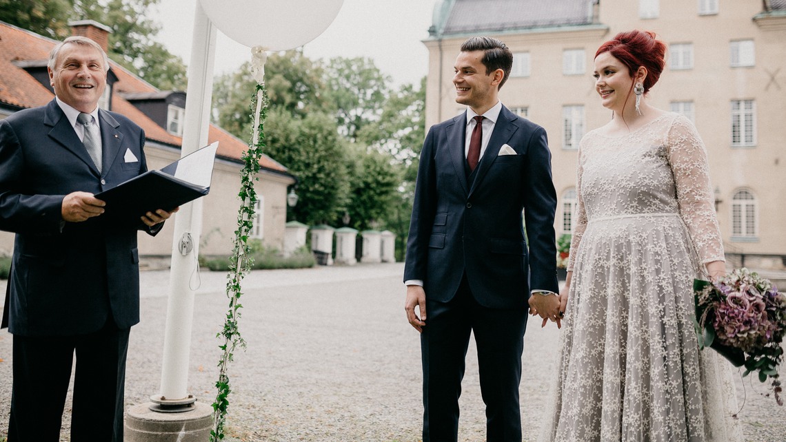 Bröllopspar framför Djursholms slott med vigselförrättare.
