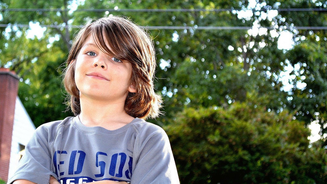 En pojke med brunt långt hår håller armarna i kors.