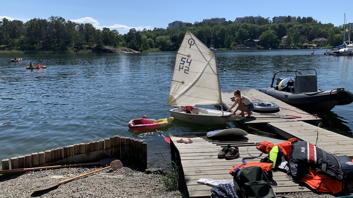 En fritidsledare sitter på bryggan i stocksunds hamn och tar in en optimistjolle. I vattnet ser vi barn paddla i kajaker och kanoter, och på bryggan ligger åror, flytvästar och skor.