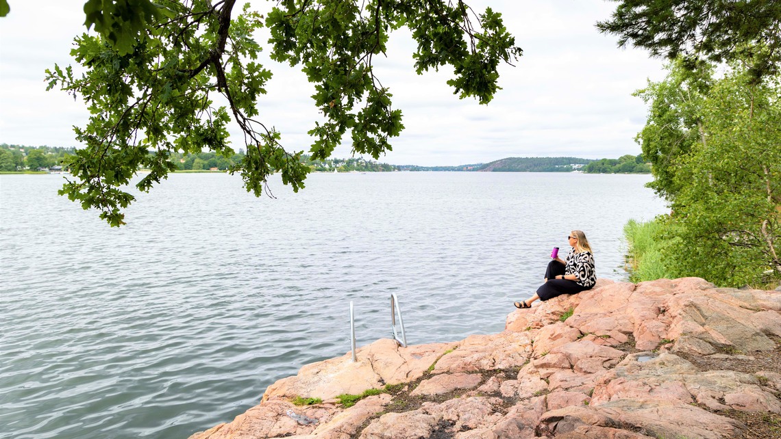 Kvinna sitter på klipporna invid badstege.