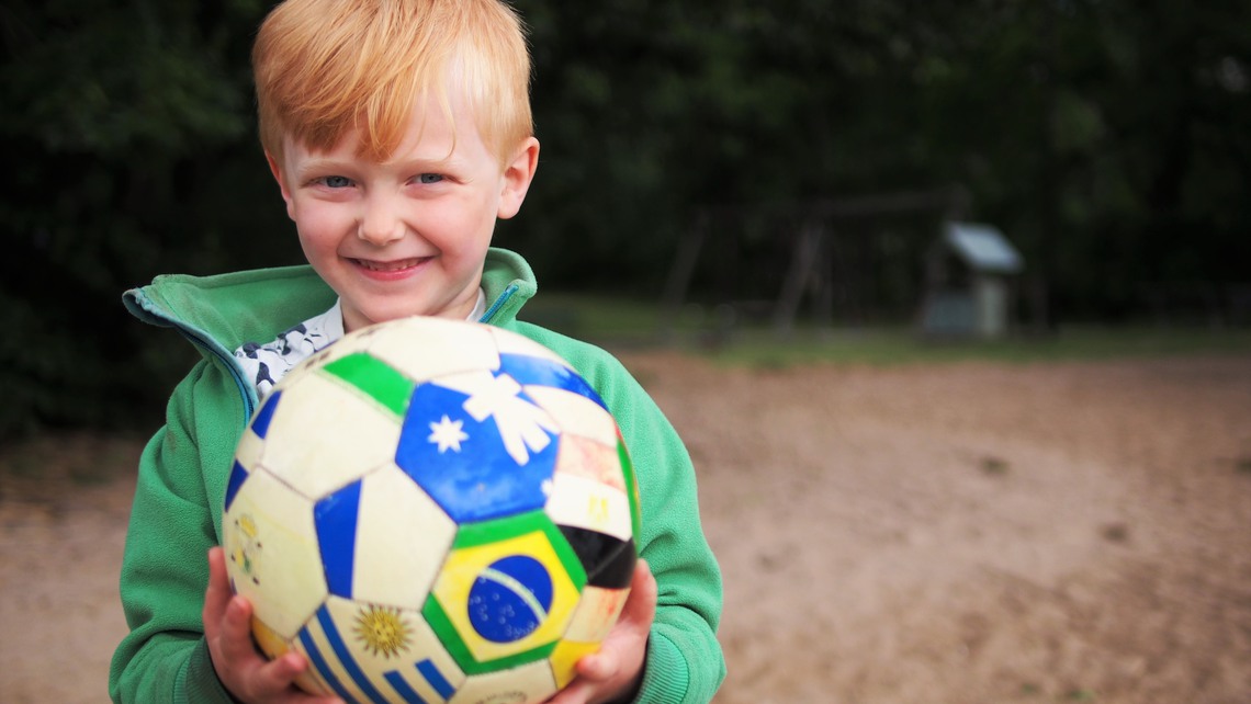 Glad pojke håller i en fotboll.